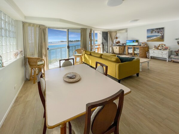 A spacious living area with a dining table, yellow sofa, and a view of the sea.