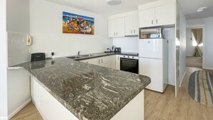 Una cocina moderna con armarios blancos, encimera de granito y refrigerador de acero inoxidable.