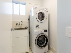 A compact laundry room with a stacked washer and dryer, a small sink with a faucet, and a window above the sink.