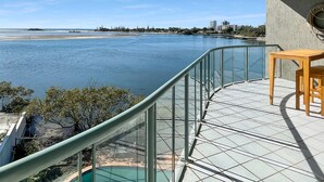 Un balcón con vistas a una gran extensión de agua, una piscina y un paisaje urbano distante.