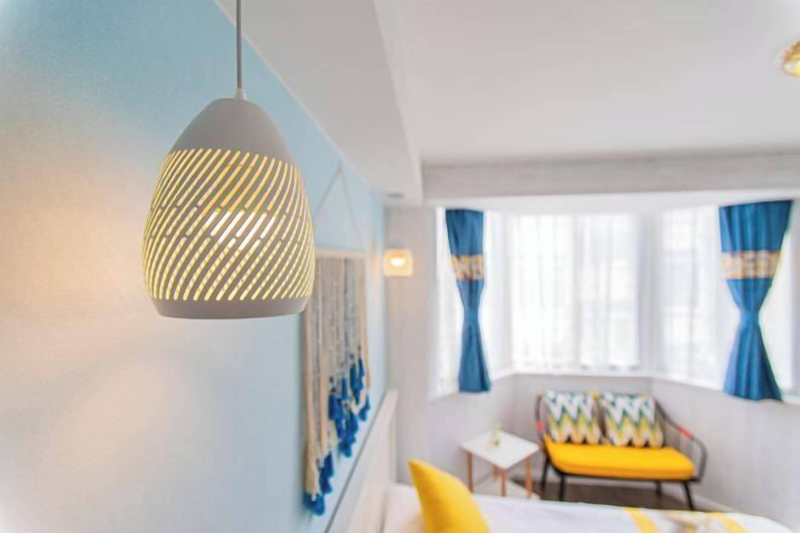 A hotel room with a bed, a chair, a small table, and a hanging light fixture.