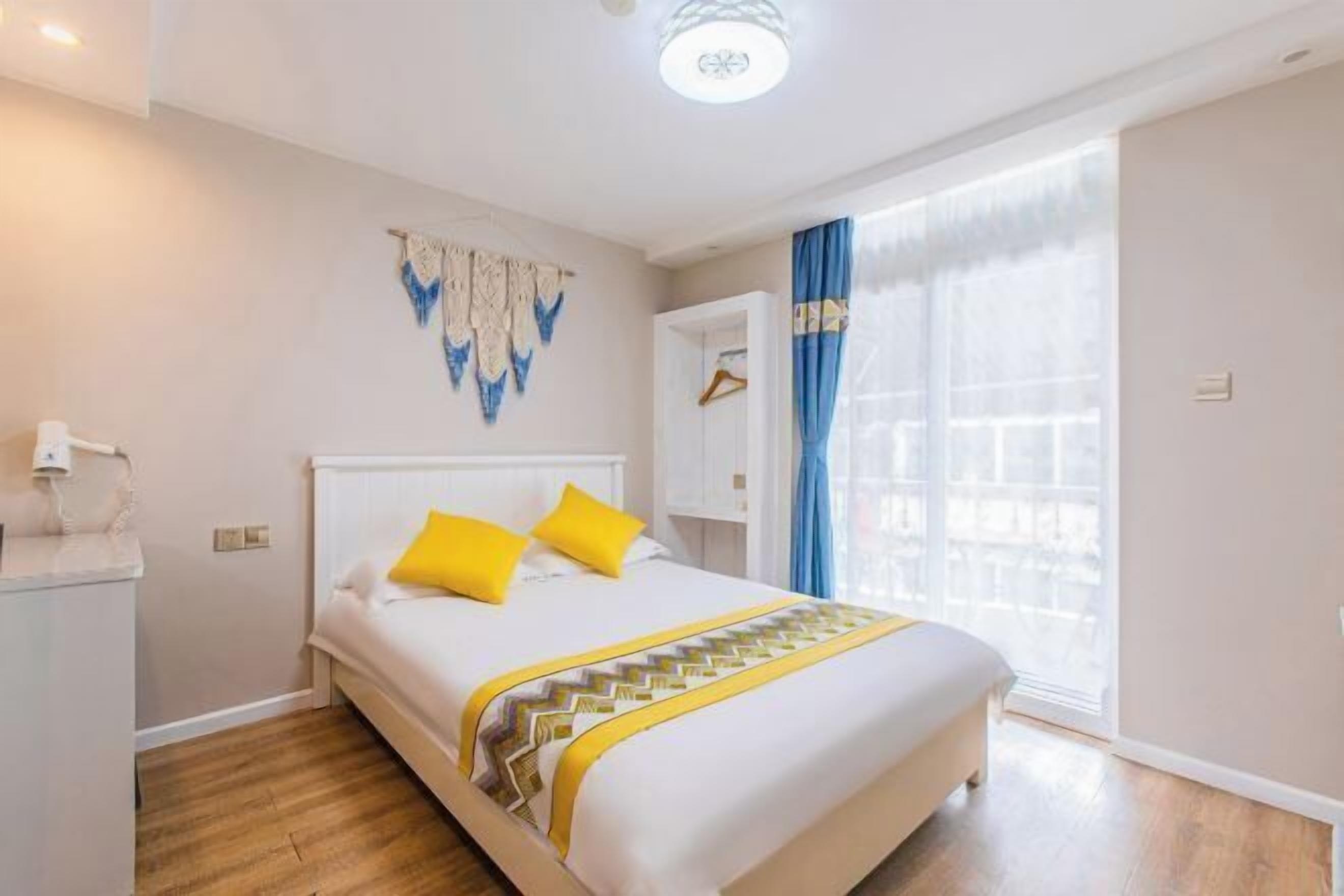 A hotel room with a bed, a bedside table, a wall-mounted light fixture, and a window with curtains.
