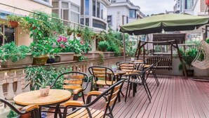 An outdoor patio with wooden tables and chairs, surrounded by lush greenery and potted plants. - Awuka Guesthouse (Hangzhou)