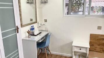 A small room with a desk, chair, and a bed. There is a window with a view of plants outside.