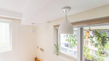 Una habitación con cama, ventana con vistas a plantas y edificios, y una lámpara colgante.