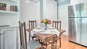 Een eethoek met een houten tafel voor vier personen, omringd door stoelen. Op tafel staat een vaas met bloemen, en rechts bevindt zich een roestvrijstalen koelkast.