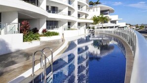 A modern hotel with a curved infinity pool, white balconies, and tropical landscaping.