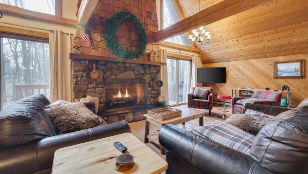 A cozy log cabin interior with a stone fireplace, leather sofas, and a television. - Mountain chalet with 6 BR, hot tub, game room and fire pit. (Lake Harmony)