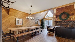 A spacious dining area with a long wooden table and benches, a fireplace, and a Christmas tree. - Mountain chalet with 6 BR, hot tub, game room and fire pit. (Lake Harmony)