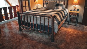 A bedroom with a wooden bed, two bedside lamps, a small table with a clock, and a view of a wooden balcony. - Mountain chalet with 6 BR, hot tub, game room and fire pit. (Lake Harmony)