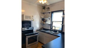 A kitchen with a black countertop, stainless steel appliances, and a sign that reads "Welcome to Farmhouse." - Entire house for fishing, hunting, or passing by! (Fairfax)