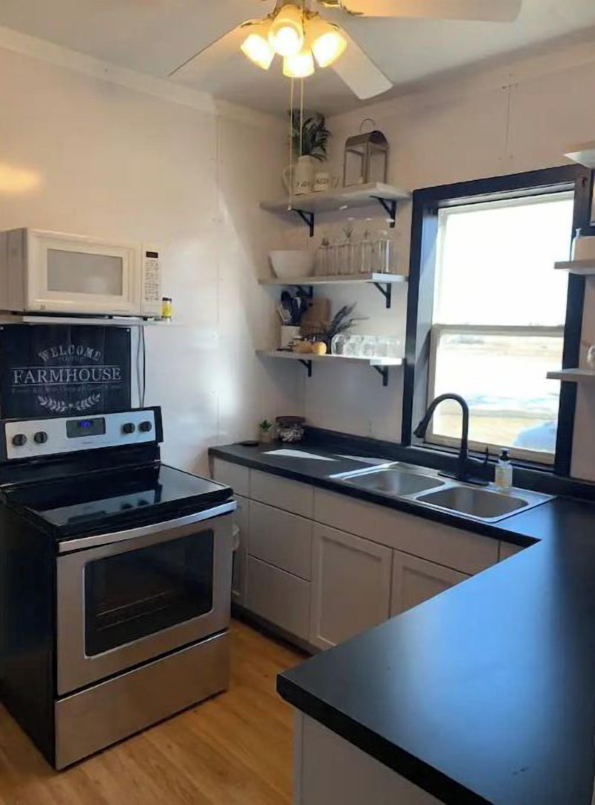 A kitchen with a black countertop, stainless steel appliances, and a sign that reads "Welcome to Farmhouse."