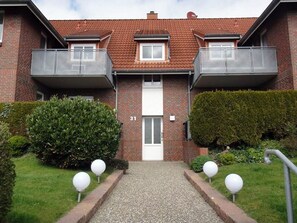 Ein zweistöckiges Backsteingebäude mit einem zentralen Eingang, zwei Balkonen im Obergeschoss und einem kleinen Fenster im zweiten Stock.
