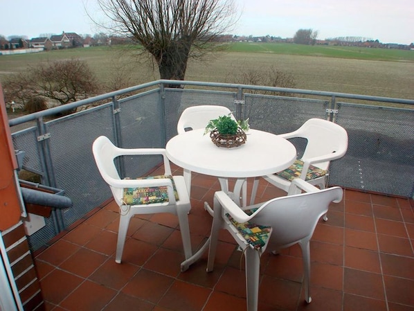A balcony with a round table and four chairs, a small plant on the table, and a view of a rural landscape.