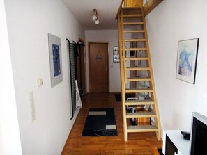 Un couloir étroit avec une échelle en bois, une porte et un tableau encadré accroché au mur.