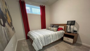 Ein Schlafzimmer mit einem Bett, einem Nachttisch, einer Lampe und einem Fenster mit roten Vorhängen.