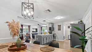 Una cocina moderna con armarios grises, un refrigerador de acero inoxidable y un comedor con una mesa de madera y individuales tejidos.