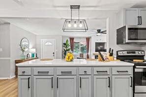 A modern kitchen with white cabinets, a central island, a microwave, and a stove.