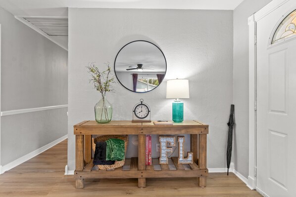 A hallway with a wooden console table, a round mirror, a clock, a lamp, and an umbrella leaning against the wall.
