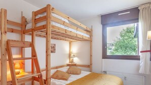 Une chambre avec un lit superposé, une échelle, une table de chevet avec une lampe et une fenêtre avec des rideaux.