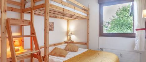 A bunk bed room with a ladder, a bedside table with a lamp, and a window with curtains.