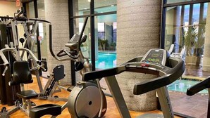 A gym with various exercise machines, a treadmill, and a view of an outdoor pool through large windows. - 2017 Top Floor Condo Of SugarTop Resort w/ Pool, Hot Tub, Breathtaking Views (Sugar Mountain)