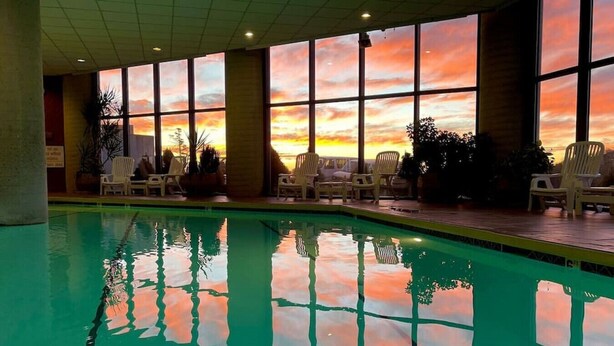 A swimming pool with clear water reflecting the sunset sky, surrounded by lounge chairs and large windows. - 2017 Top Floor Condo Of SugarTop Resort w/ Pool, Hot Tub, Breathtaking Views (Sugar Mountain)