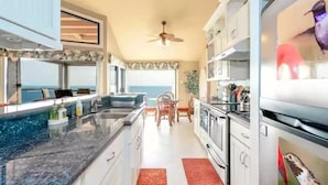 Een moderne keuken met een groot eiland, witte kasten en uitzicht op zee.