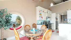 Een moderne keuken met witte kastjes, een centraal eiland en een eetgedeelte met een glazen tafel en rieten stoelen.
