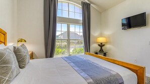 A hotel room with a bed, a TV mounted on the wall, a window with curtains, and a lamp on a side table. - Large Home near Theme Parks with Pool, Spa and Pets Welcome! (Kissimmee)