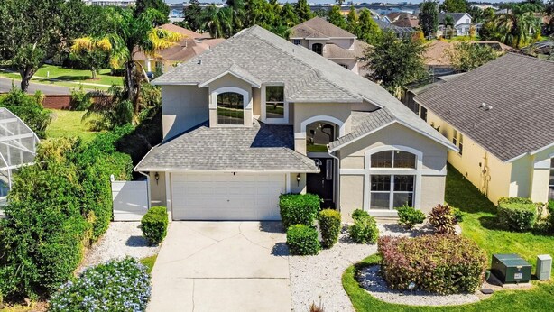 A two-story house with a garage, surrounded by well-maintained lawns and mature trees. - Large Home near Theme Parks with Pool, Spa and Pets Welcome! (Kissimmee)