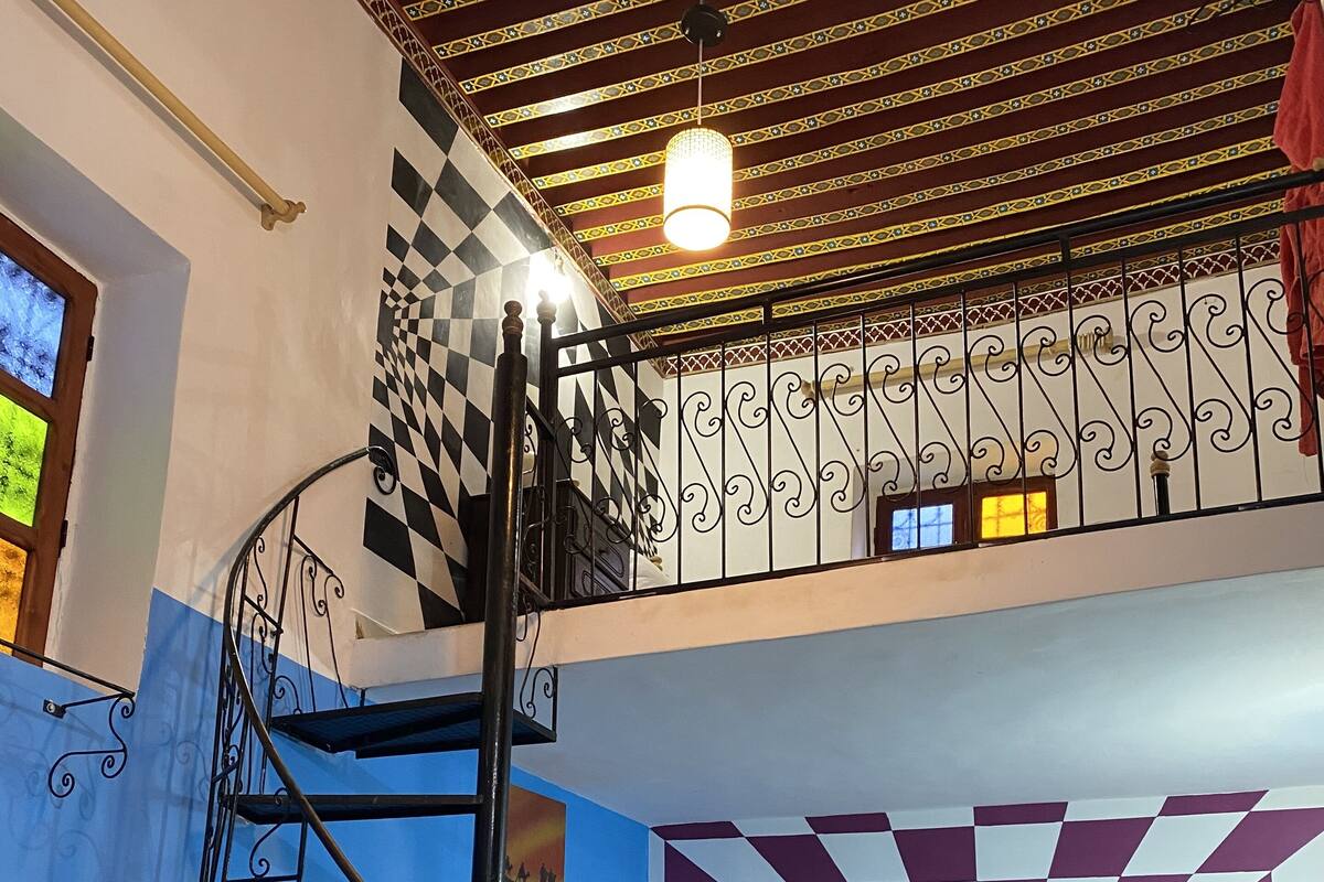 Una habitación con pared a cuadros, una escalera de caracol y una cama con almohada a cuadros.