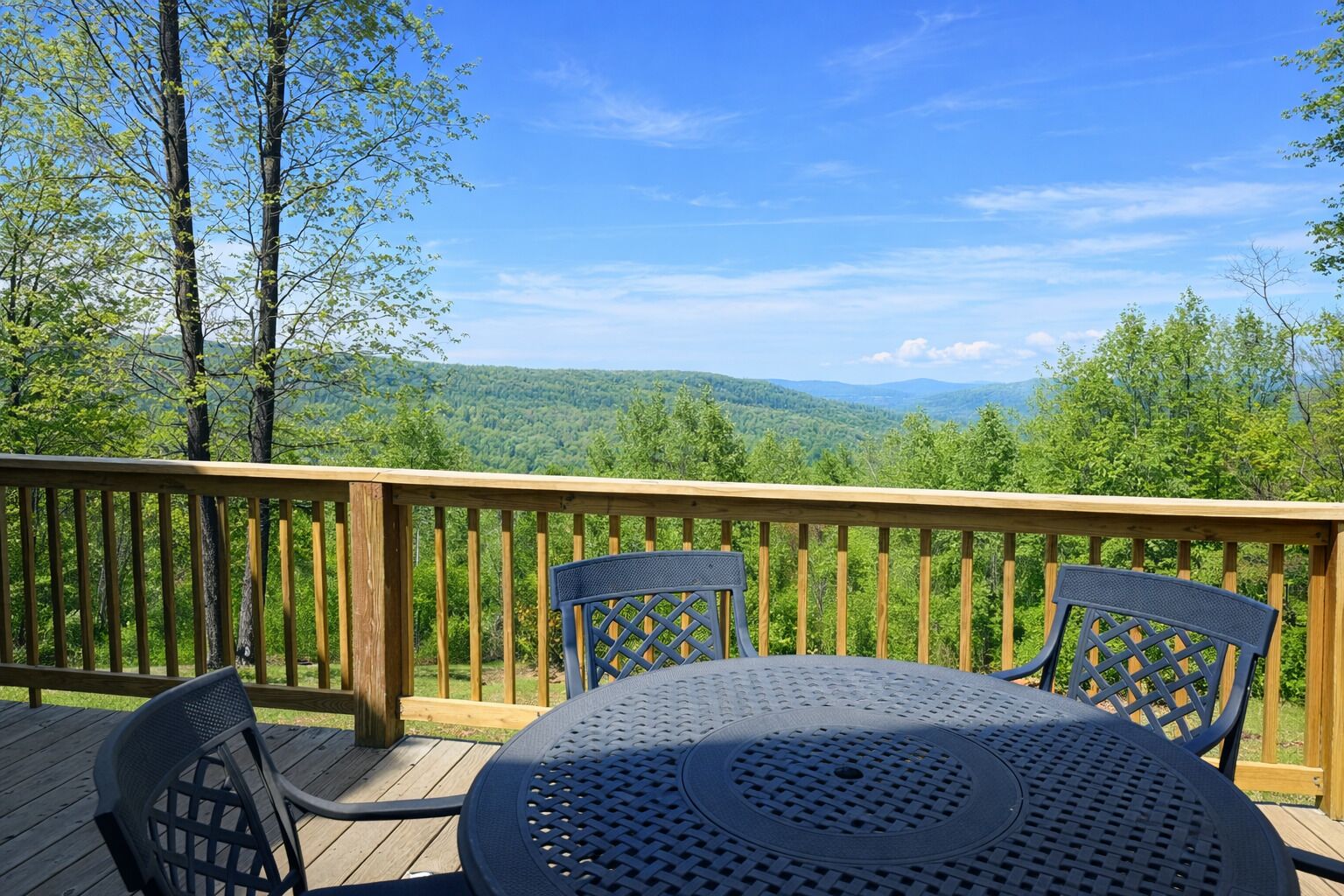 A deck with a table and chairs, overlooking a forested landscape.