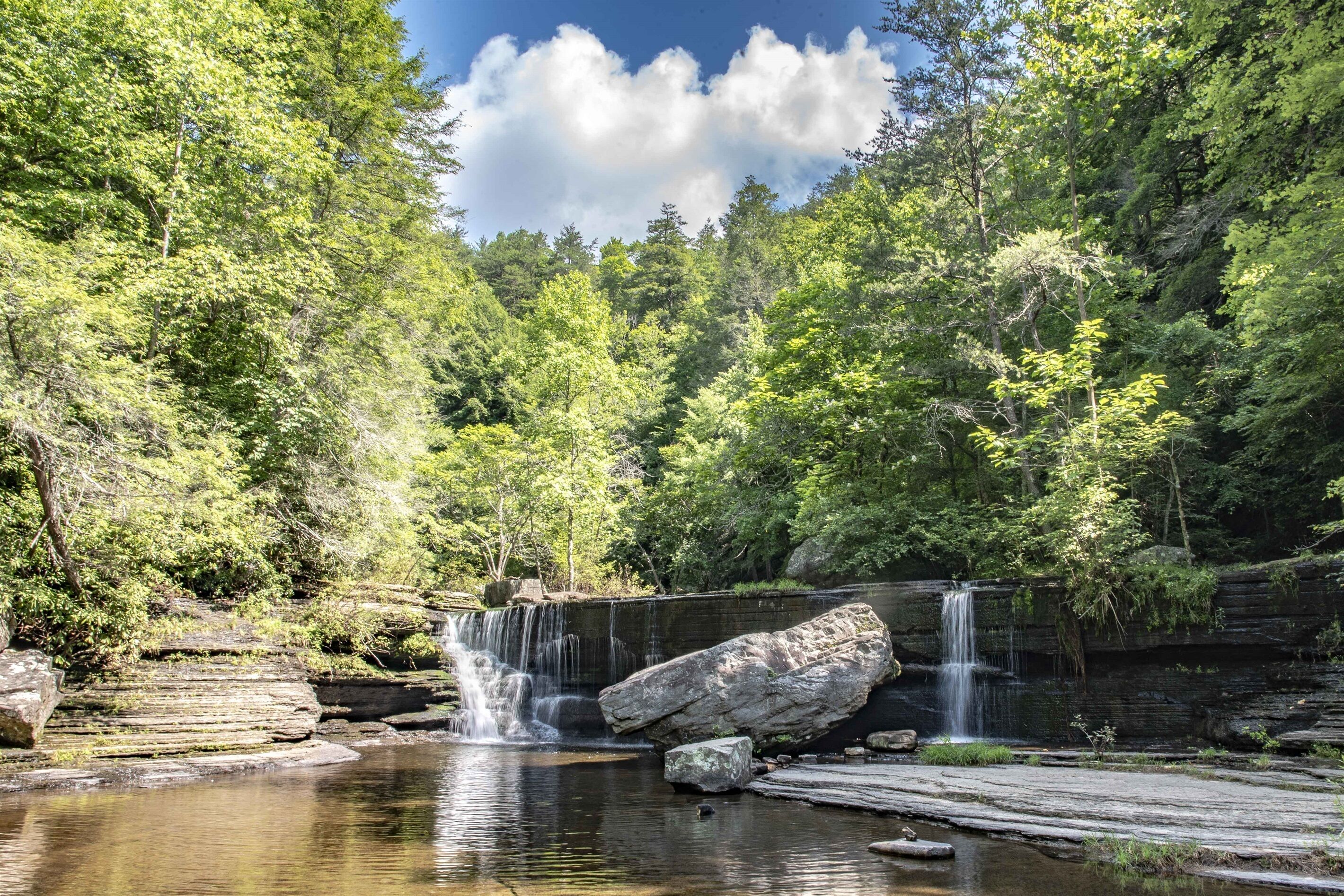 Eine natürliche Landschaft mit einem Wasserfall, felsigem Gelände und dichtem Wald.