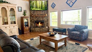 A living room with a stone fireplace, a television mounted above it, a leather sofa, a patterned armchair, and a coffee table with a bowl. - Stone's Mountain View (Altamont)