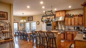 A spacious kitchen with wooden cabinets, a central island with bar stools, and a dining area with a metal table and chairs. - Stone's Mountain View (Altamont)
