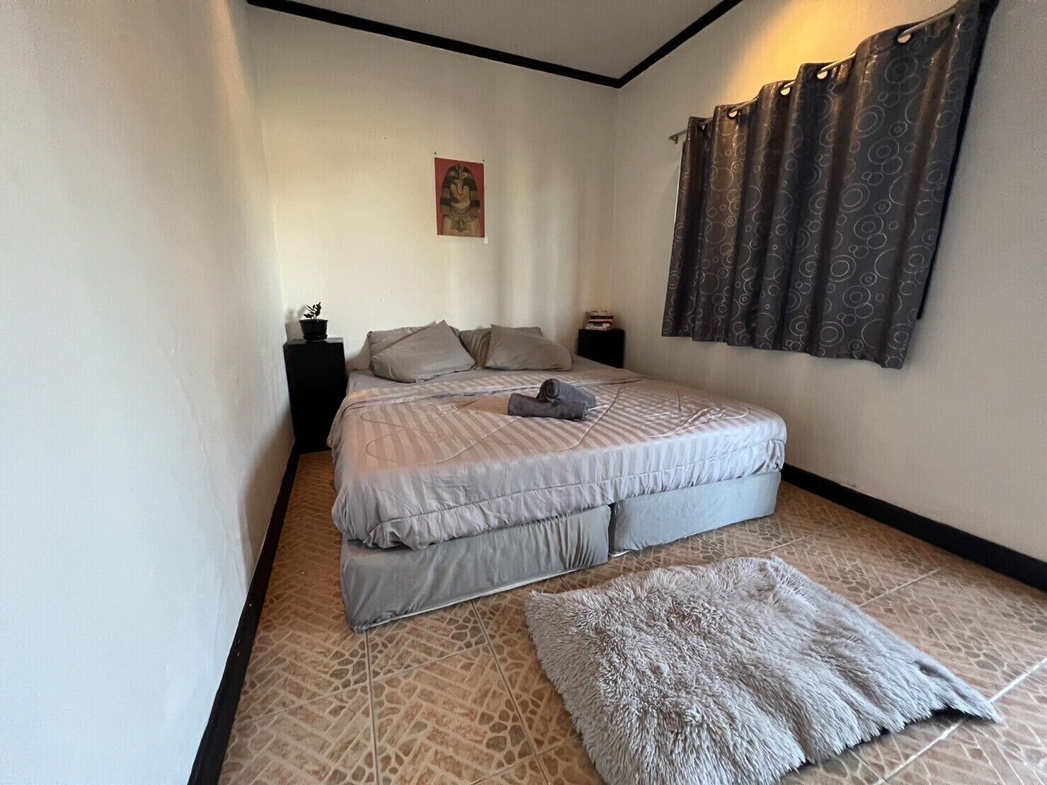 Un dormitorio con una cama grande, una mesita de noche pequeña, un cuadro en la pared y una cortina estampada.