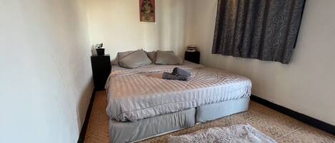 Un dormitorio con una cama grande, una mesita de noche pequeña, un cuadro en la pared y una cortina estampada.