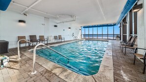 An indoor swimming pool with a view of the ocean, surrounded by lounge chairs and a tiled floor. - ⛱️SummerChase 904⛱️ indoor pool, hot tub, kiddie pool, gym, and beach towels (Orange Beach)