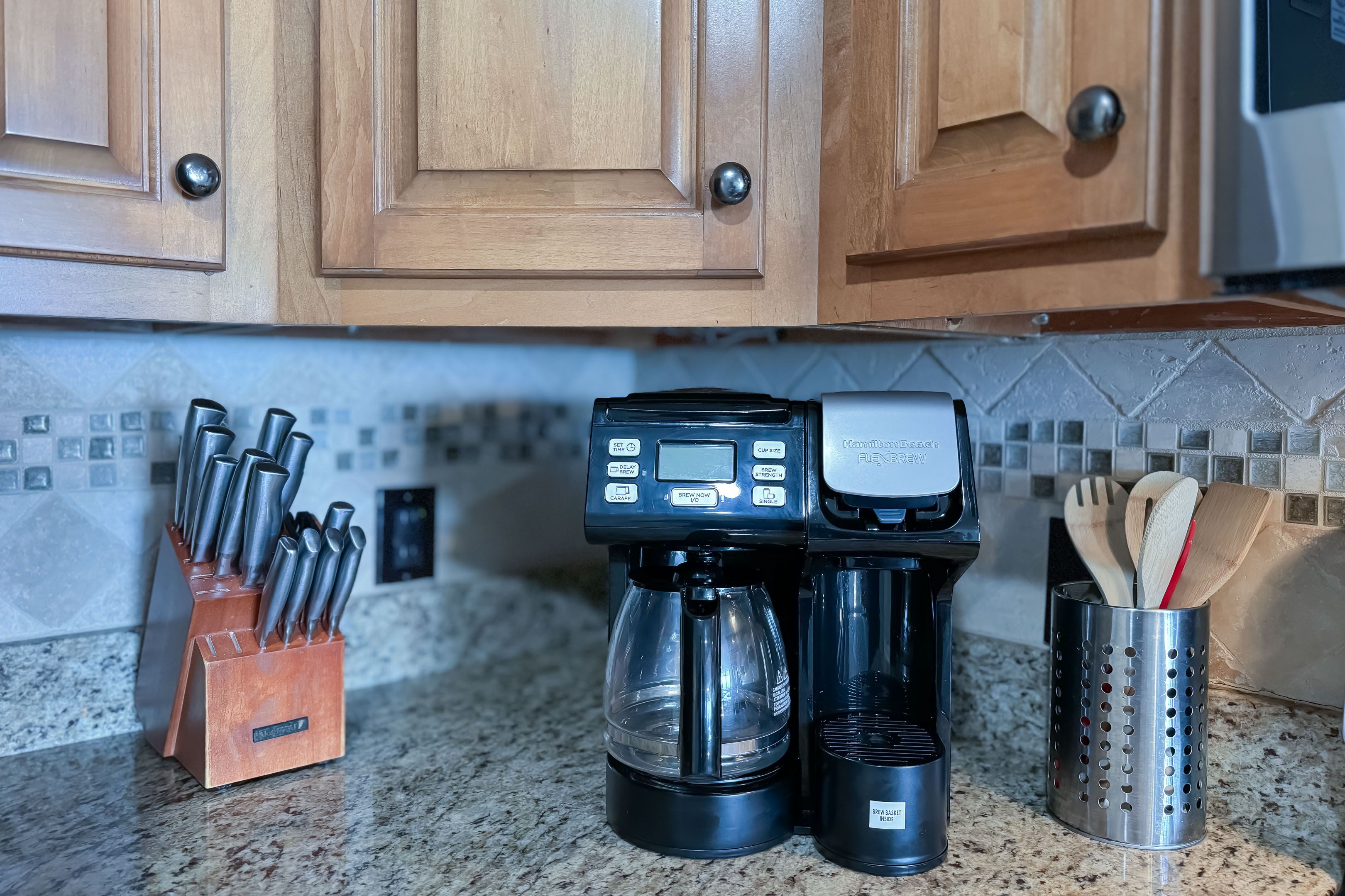 A kitchen with wooden cabinets, a coffee maker, a knife block, and a utensil holder.