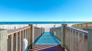 A wooden boardwalk leading to a beach with a clear blue sky. - ⛱️SummerChase 904⛱️ indoor pool, hot tub, kiddie pool, gym, and beach towels (Orange Beach)