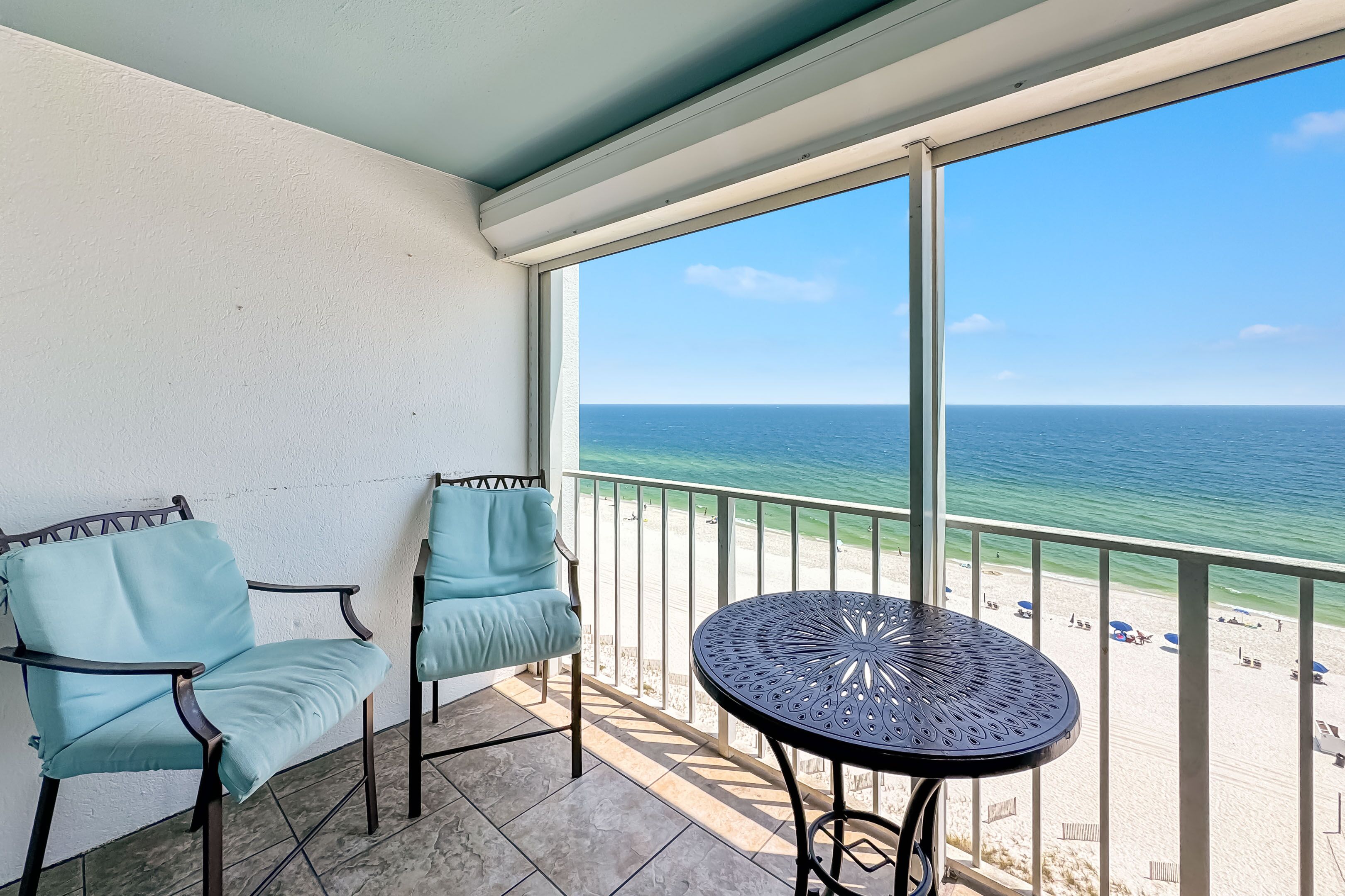 A balcony with two chairs and a table, overlooking a beach with a clear view of the ocean.