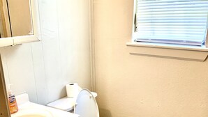 A bathroom with a toilet, sink, and cabinet. - The Ugly House (Houston)