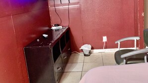 A small room with a bed, a TV mounted on the wall, a wooden dresser, and a chair. - The Ugly House (Houston)