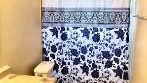 A bathroom with a toilet, sink, and shower curtain with a floral pattern. - The Ugly House (Houston)