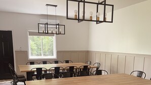A dining area with a large wooden table and black chairs, a pendant light fixture, and a window with a view of greenery.