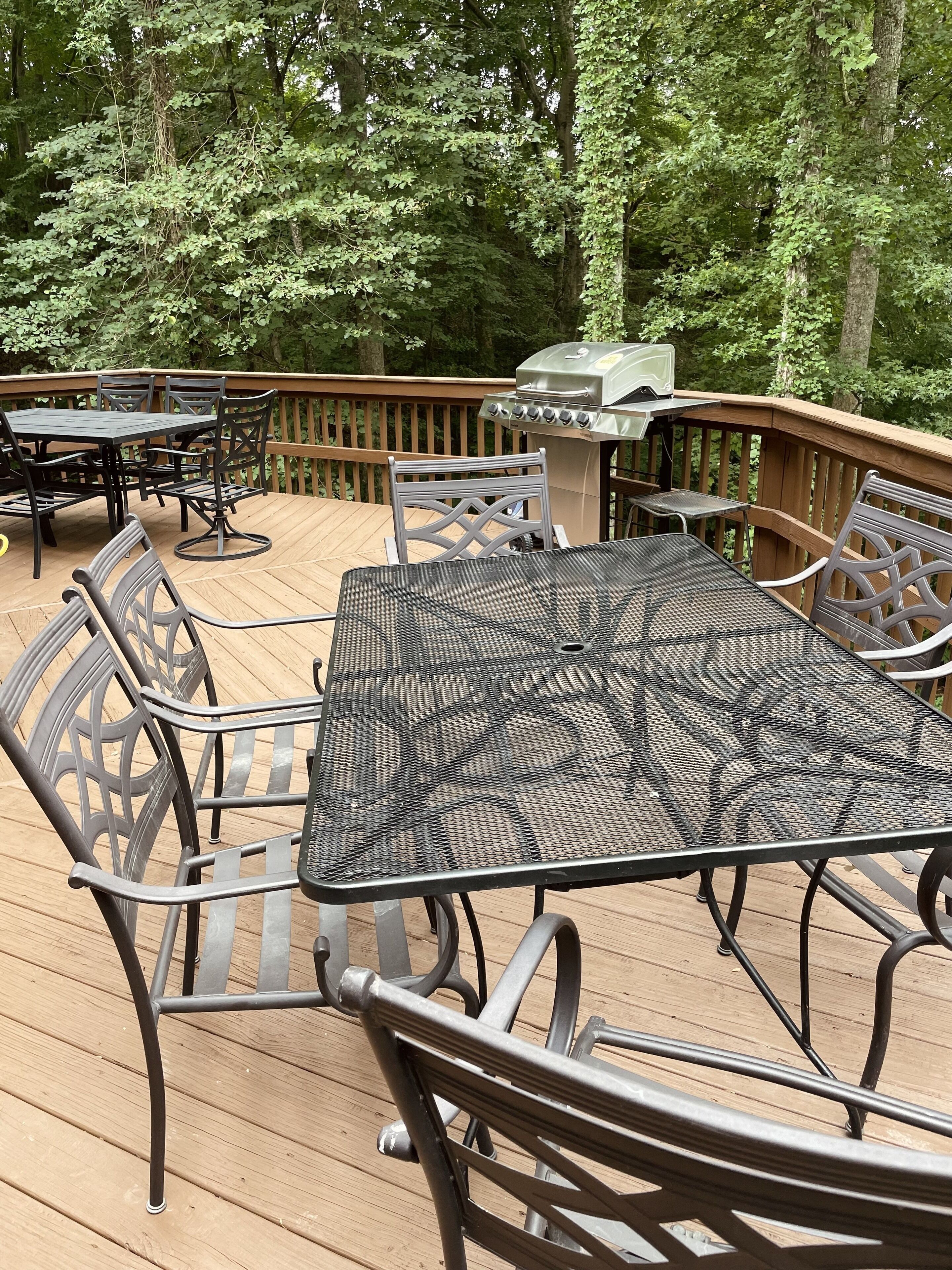 Una terraza al aire libre con una mesa y sillas de metal, rodeada por una cubierta de madera y una parrilla.