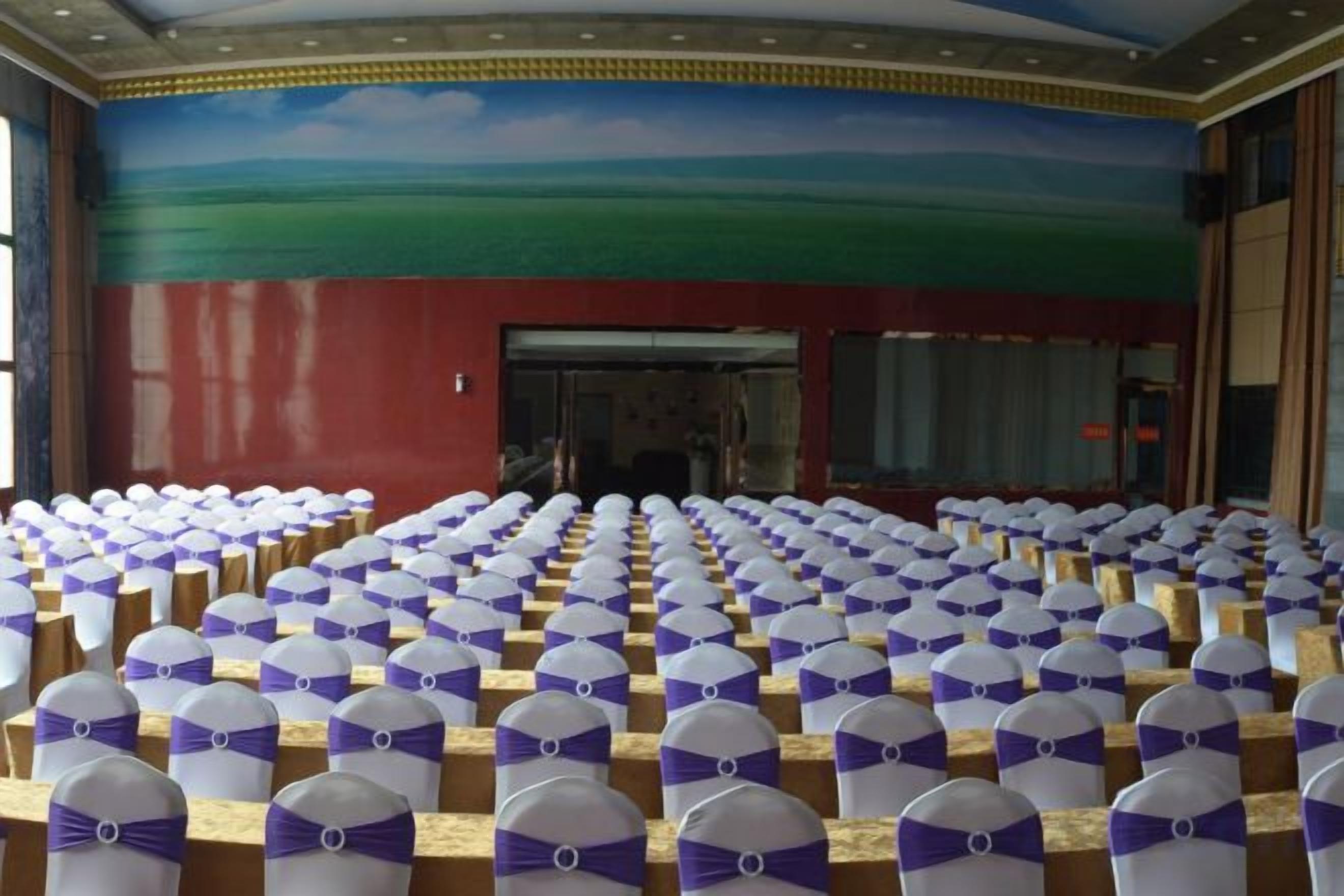 A large hall with rows of chairs, each with a white cover and a purple ribbon.