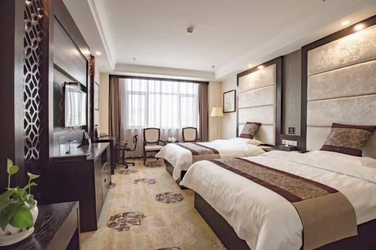 A hotel room with two beds, a desk, a chair, and a large window.