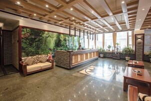 A hotel lobby with a reception desk, a sofa, a coffee table, and a large window with a view.